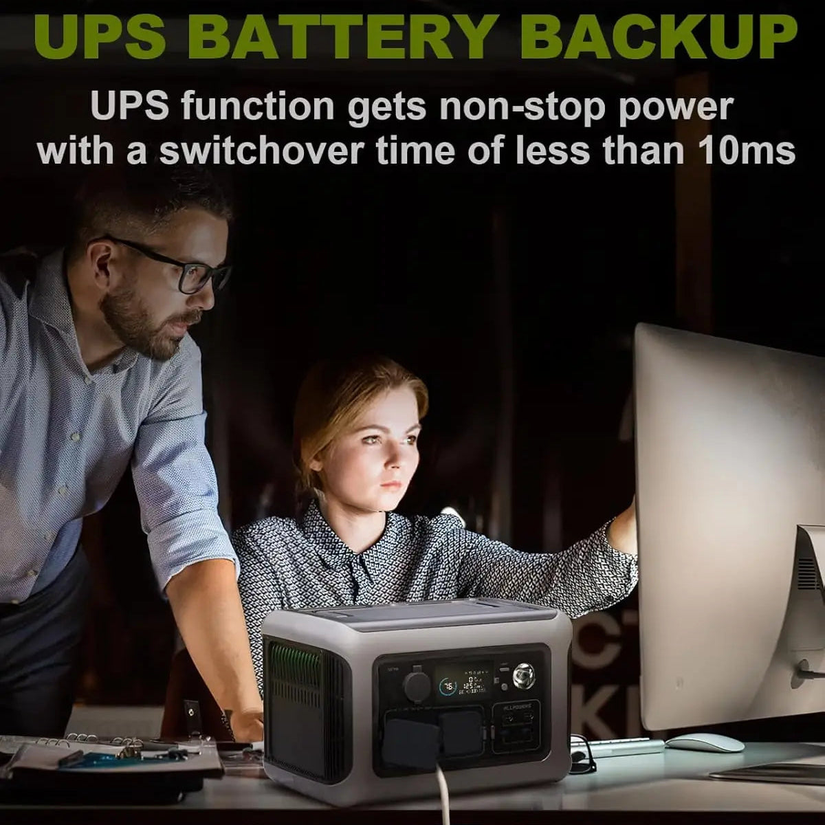 Two people using a desktop computer powered by a UPS battery backup in a dark office.