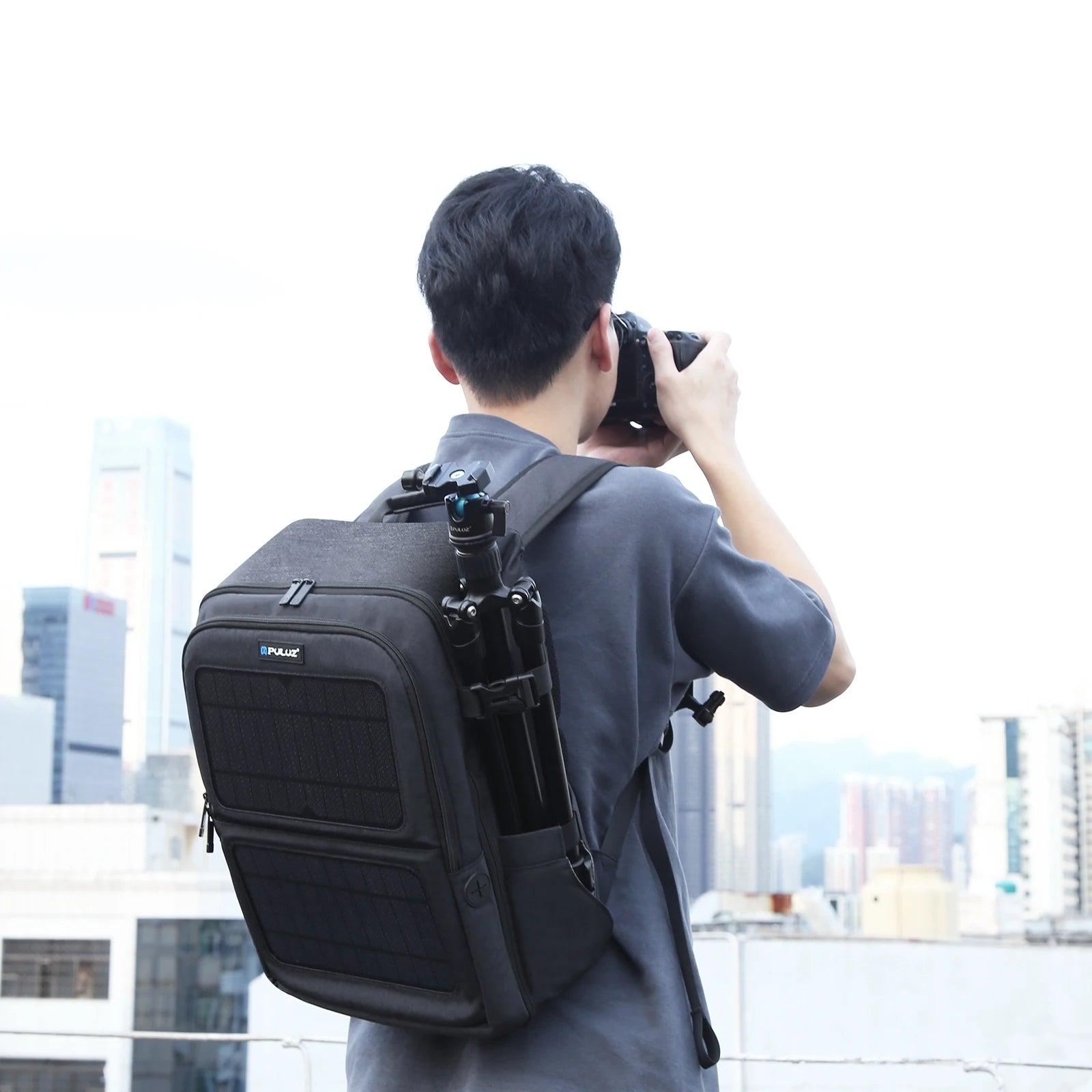 Person photographing cityscape with solar-powered camera backpack and tripod outdoors